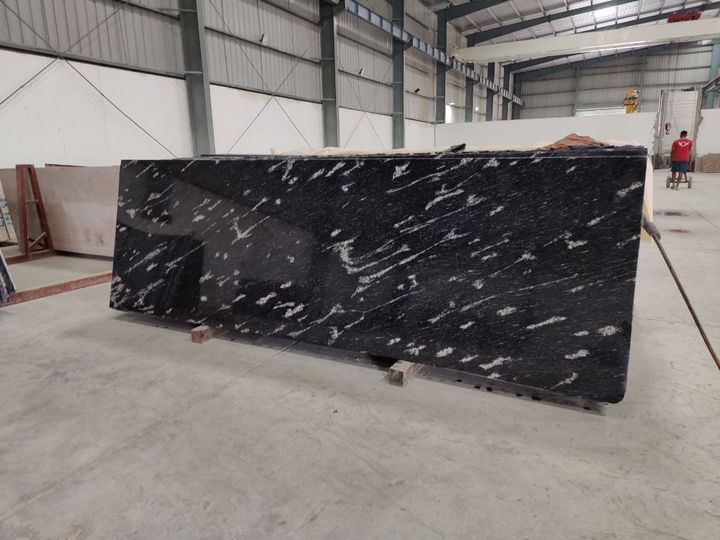 Black granite slab with bold white wave-like veins in a warehouse