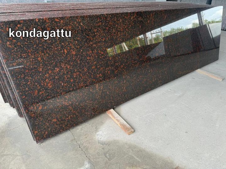 Stack of polished red-brown flecked granite slabs labelled kondagattu