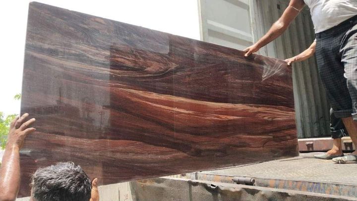 Polished teakwood granite slab with swirling wood-grain pattern being unloaded